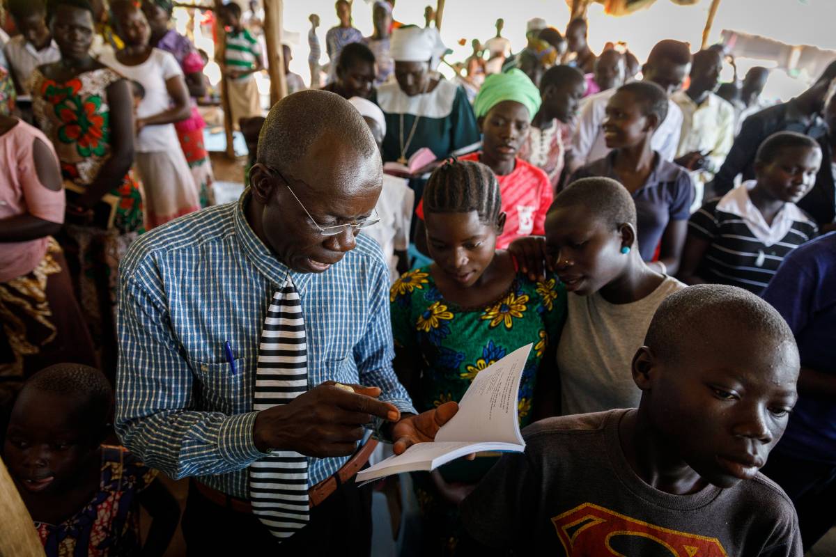Man from Uganda reading Scripture in a large group of people.